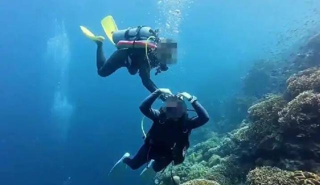 网传视频显示，一名潜水员对镜头摆出“比心”动作，身后另一名潜水员伸手对其气瓶进行操作